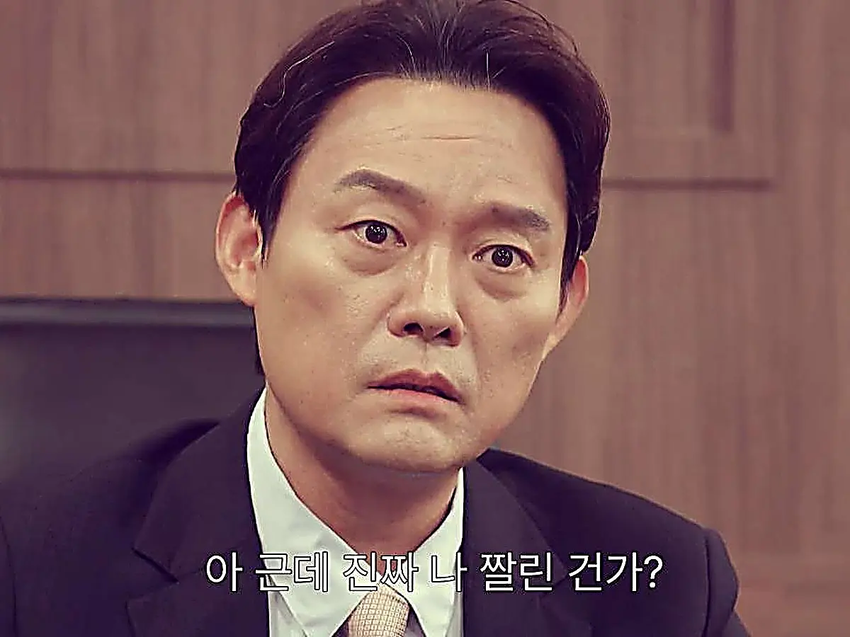 A man in a dark suit and collared shirt staring forward with wide, shocked eyes