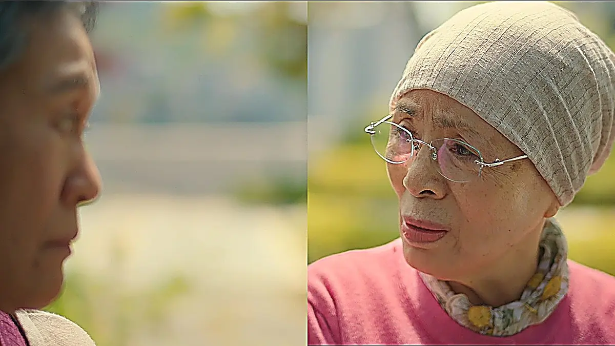 A woman wearing glasses and a knit beanie talking with another person outdoors