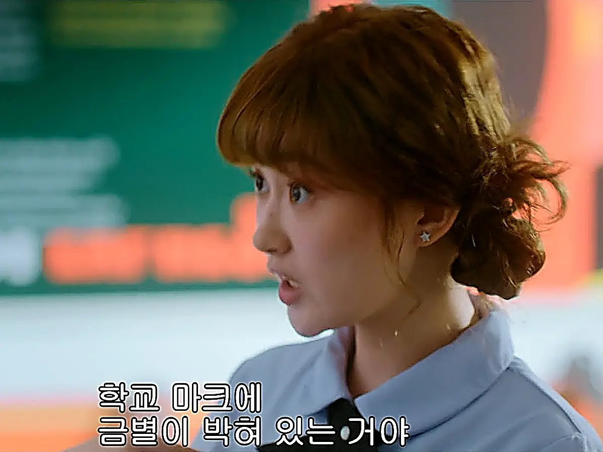 Nana speaking animatedly with brown hair styled in a bun wearing a star earring and collared uniform