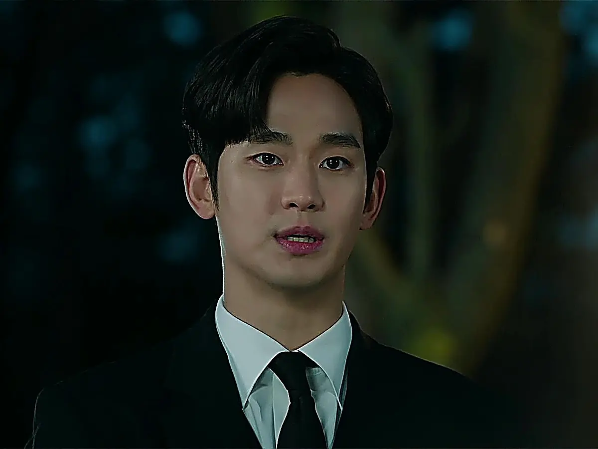 Man in a black suit and black tie looking resolute outdoors