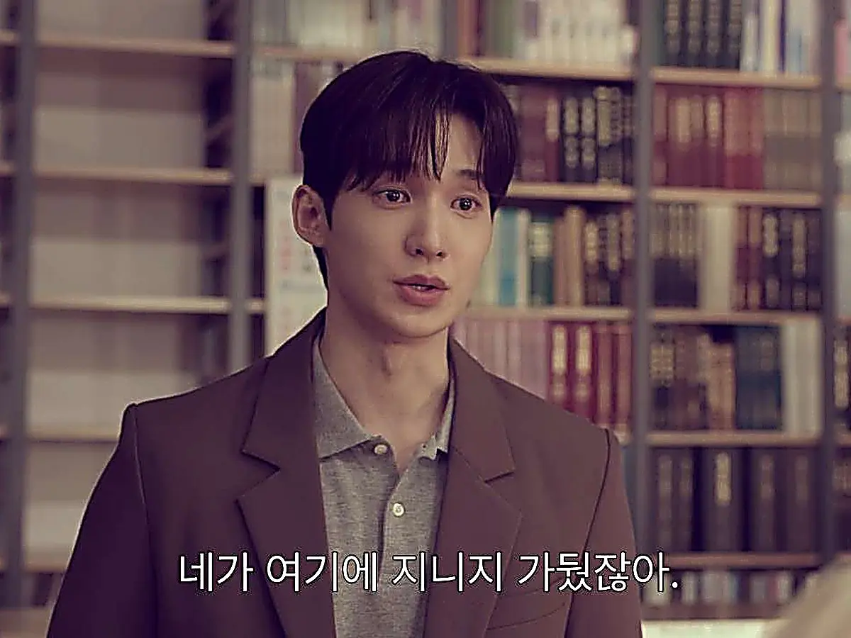 Ji-woo wearing a tailored brown blazer over a grey collared knit polo shirt