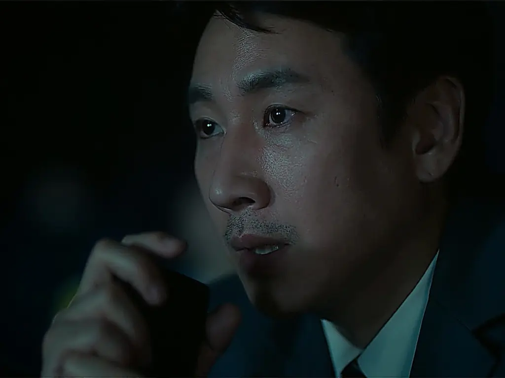 A close-up view of a man holding a phone near his face in a dimly lit car