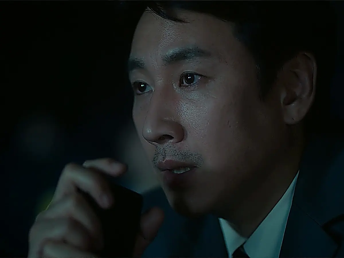 A man holding a mobile phone close to his mouth in the dark interior of a car