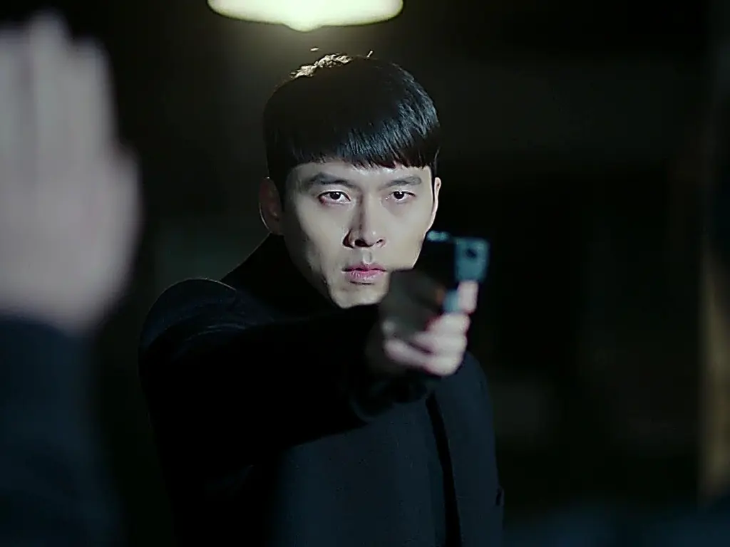 A man in a dark coat aiming a black handgun forward with an intense gaze.