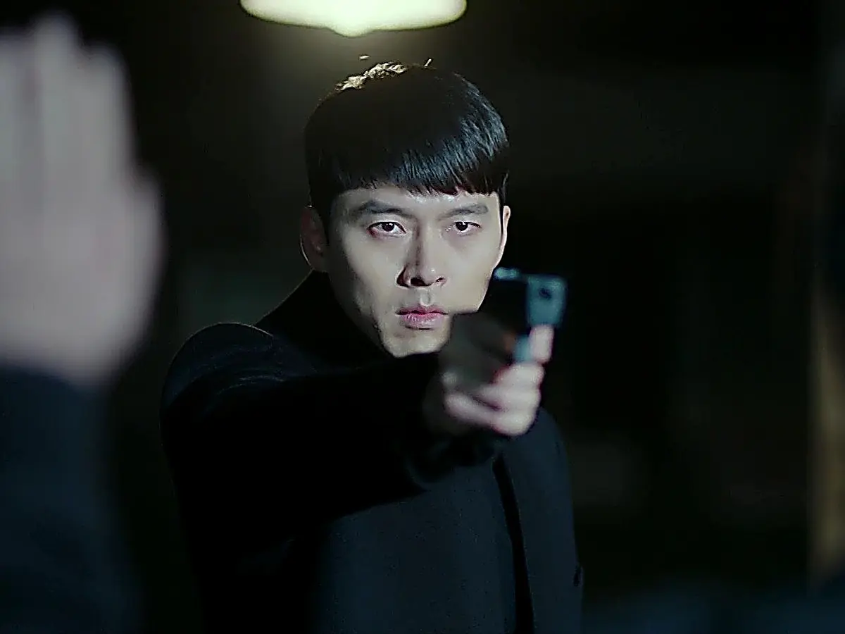 A man in a dark high-collar coat aiming a black handgun forward with an intense gaze.