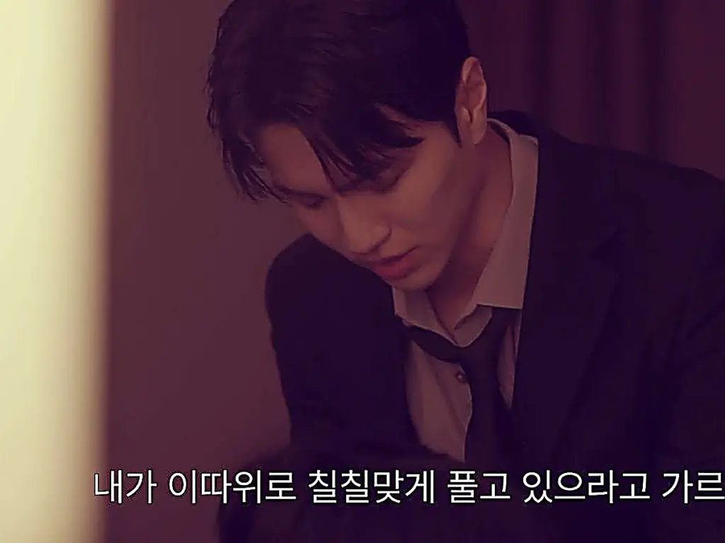 Kang Do-jin looking downward while wearing a dark tailored suit jacket over a collared dress shirt with a loosened necktie