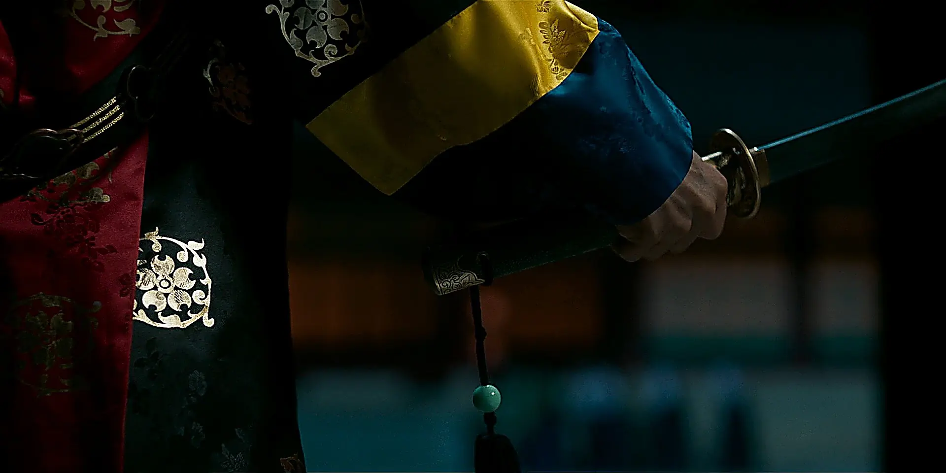 Close-up of the sword drawn from layered cobalt blue and gold stamped sleeves