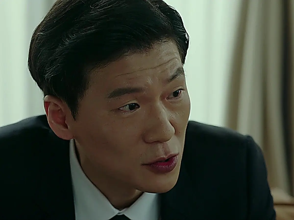 A man in a dark business suit and light dress shirt speaking with an intense expression