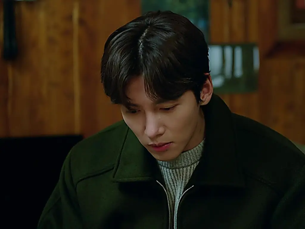 Cho Yong-pil wearing a dark forest green zip jacket layered over a textured grey knit sweater in Welcome to Samdal-ri