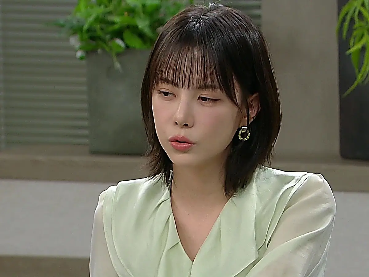 A woman with dark shoulder-length hair and bangs wearing a pale mint collared blouse looking downward.