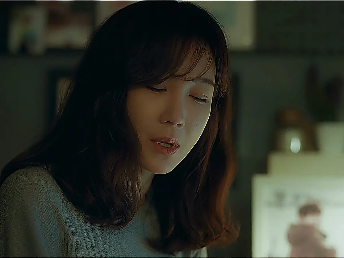 A woman with wavy shoulder-length hair looking downward in soft indoor lighting