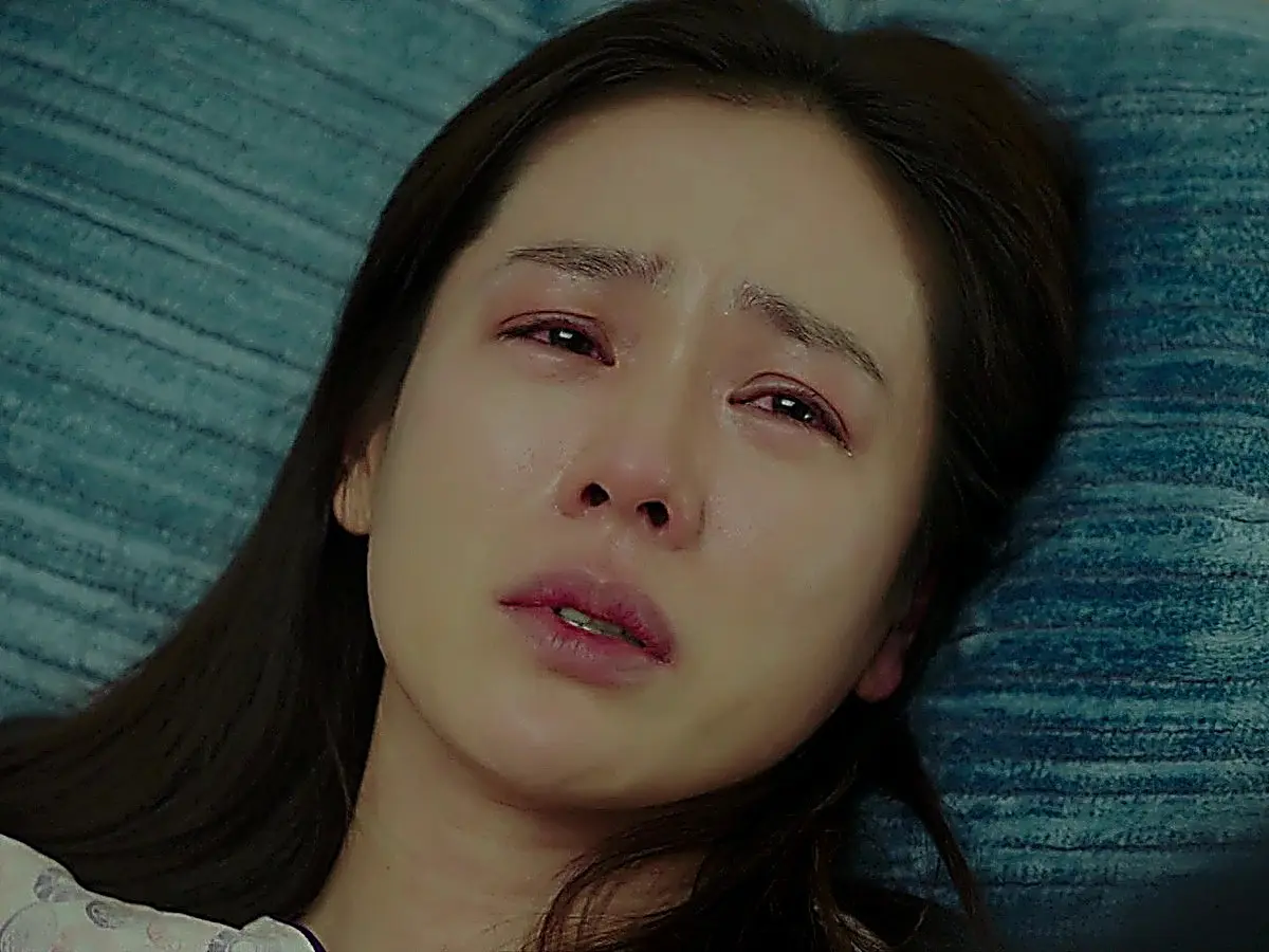 Close-up of a woman lying down on a textured blue surface with tears in her eyes