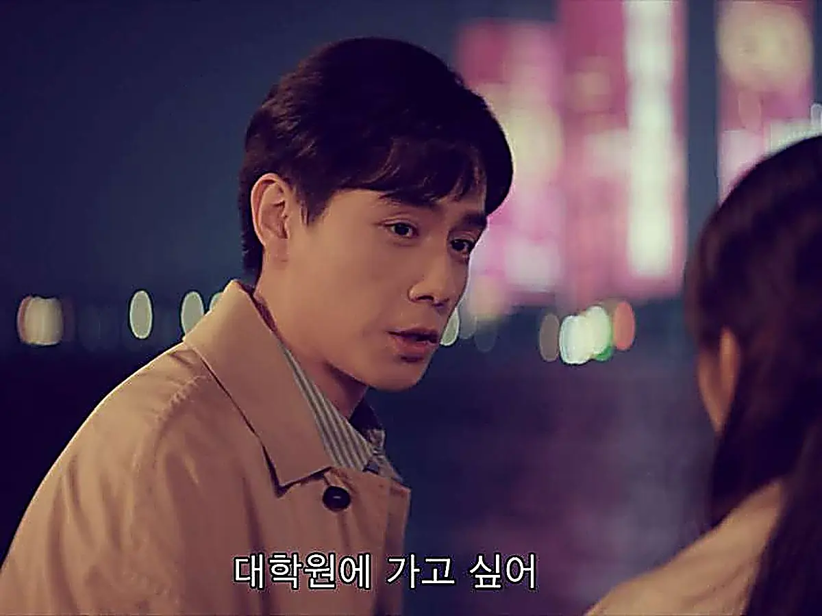 A man in a tan jacket and striped shirt speaking outdoors at night