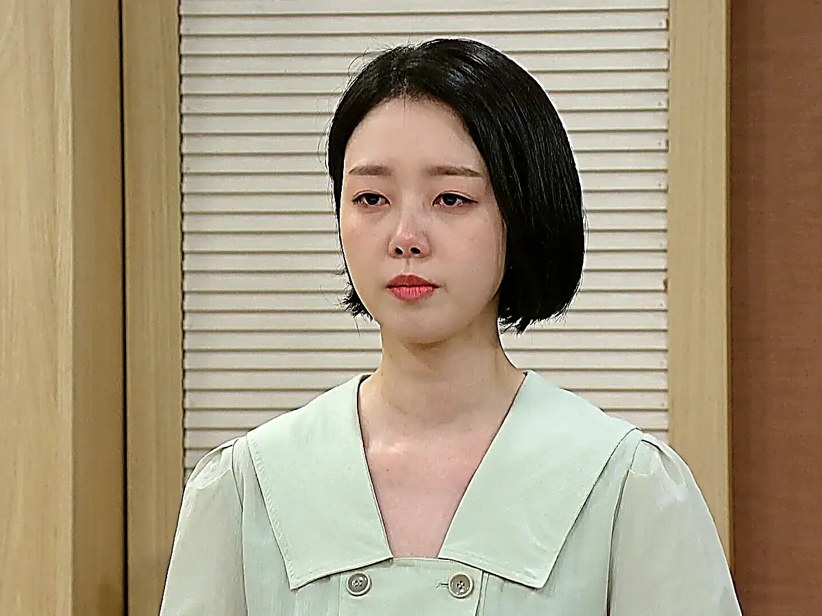 A woman with short dark hair in a light green collared blouse looking down sorrowfully
