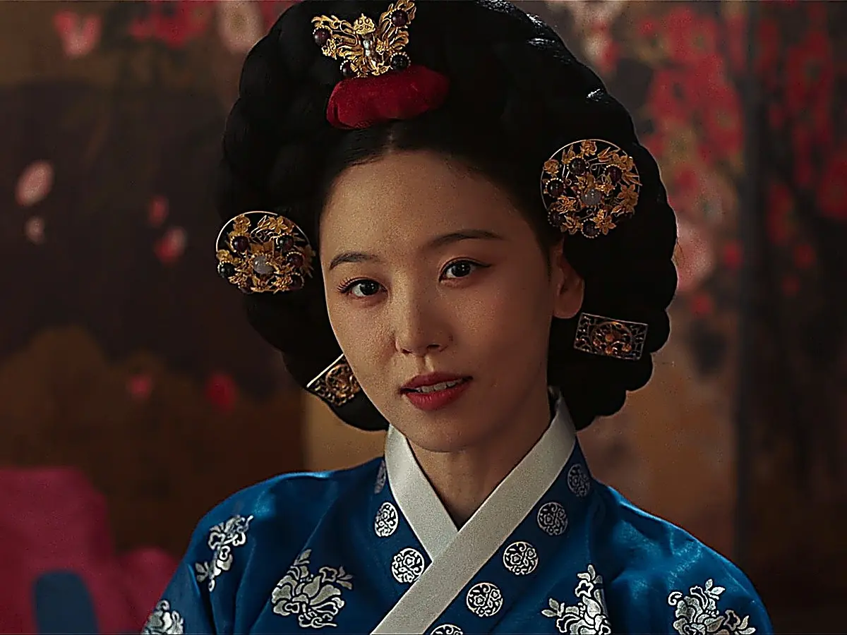 Consort Kang Mok-ju smiling coldly while adorning hair ornaments in front of her mirror