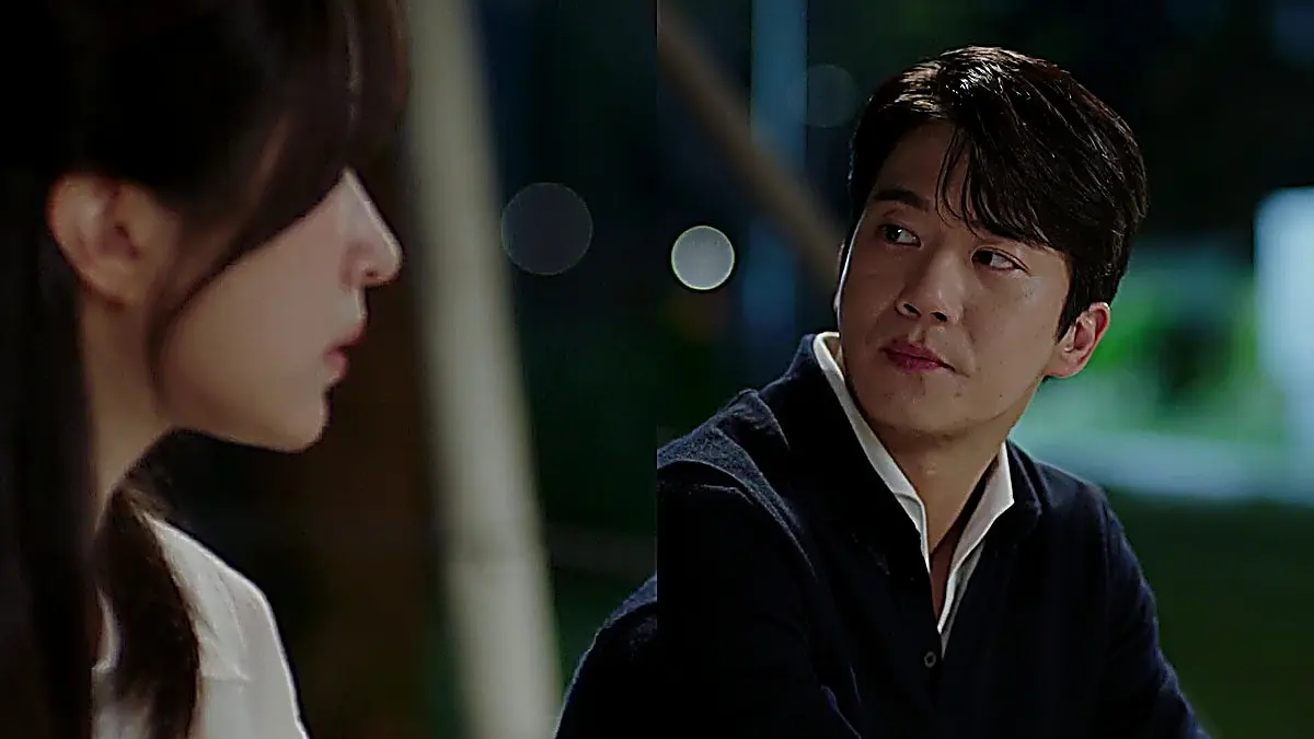 Mu-jin wearing a dark knit layer over a white collared shirt looking across a table