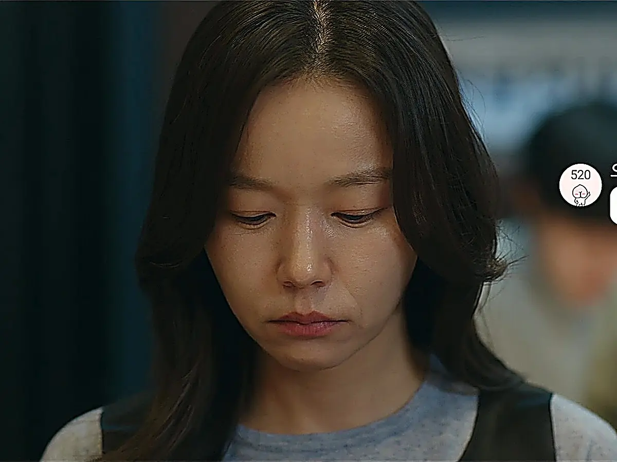 A woman with shoulder-length dark hair looking down with a subdued expression