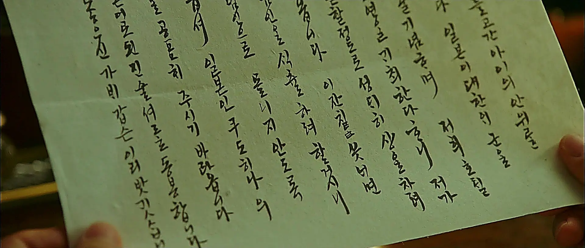 Hands holding a sheet of paper with vertical Korean calligraphy