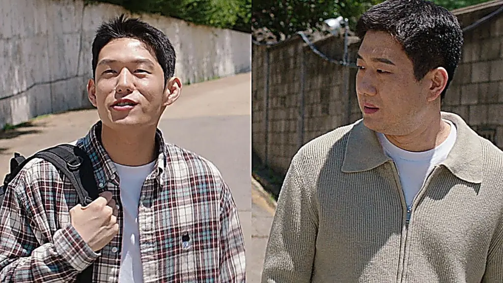 Two men in casual shirts walking outdoors along an asphalt road next to a concrete wall.