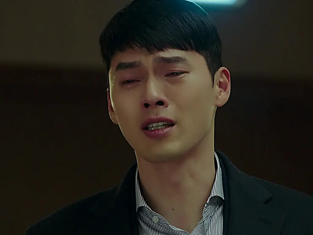 A man with short dark hair in a dark blazer crying with visible tears on his face