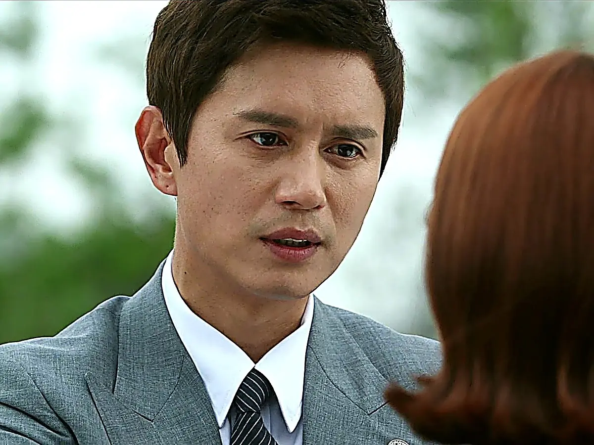 Choi Yoon in a tailored grey suit jacket with wide peak lapels and a striped tie