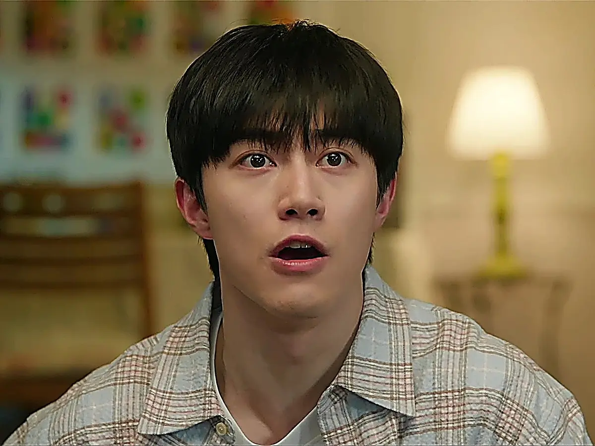 Young man in a plaid collared shirt looking upward with wide eyes indoors