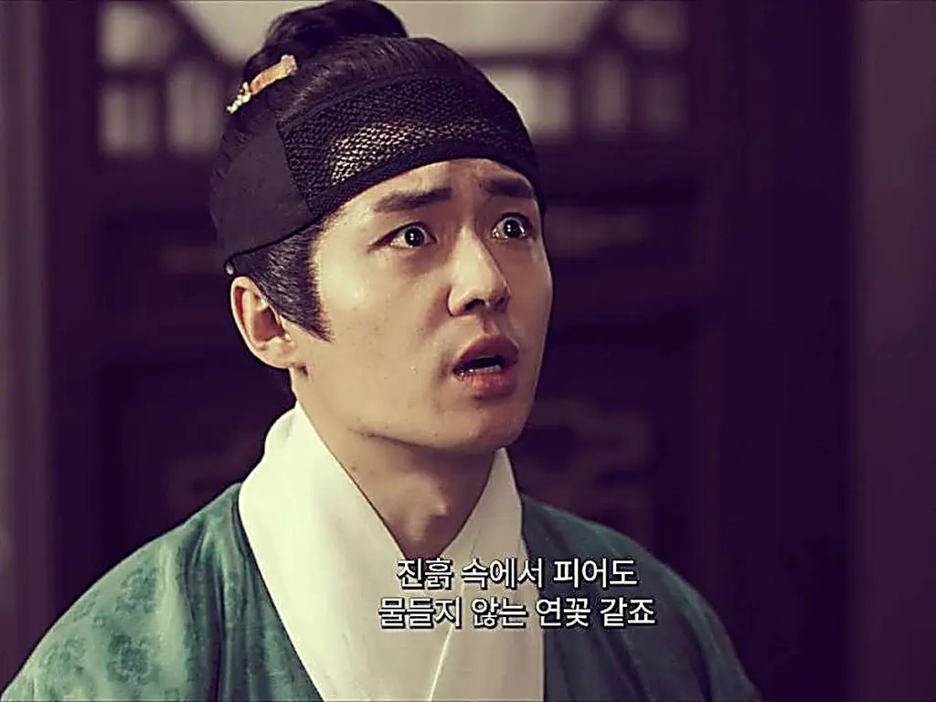 A young man wearing a green robe and black mesh headband with wide, tearful eyes