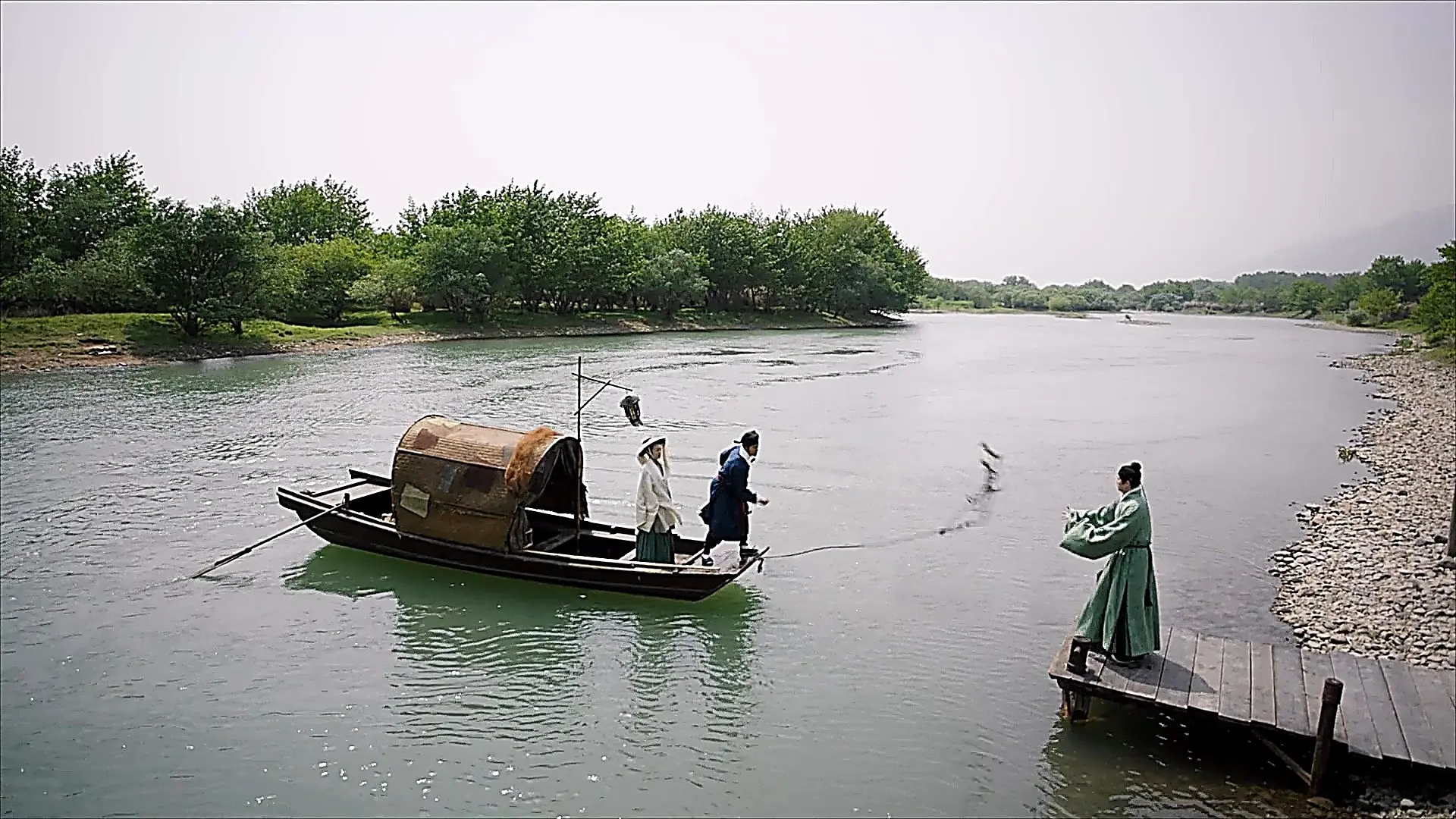 A wide river view where a person on a wooden dock throws a rope to catch a small boat