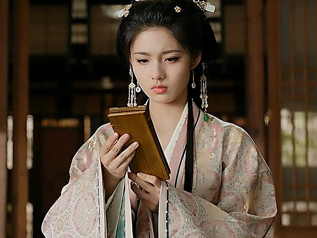 A woman in a floral patterned robe holding and examining a folded wooden plaque