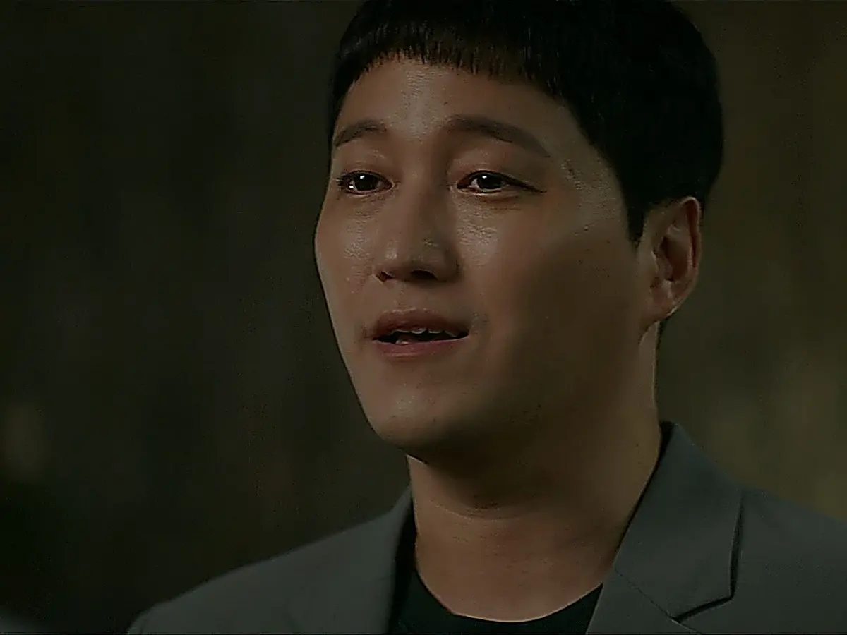 Yang Seok-hyeong outdoors speaking while wearing a grey suit jacket over a dark t-shirt