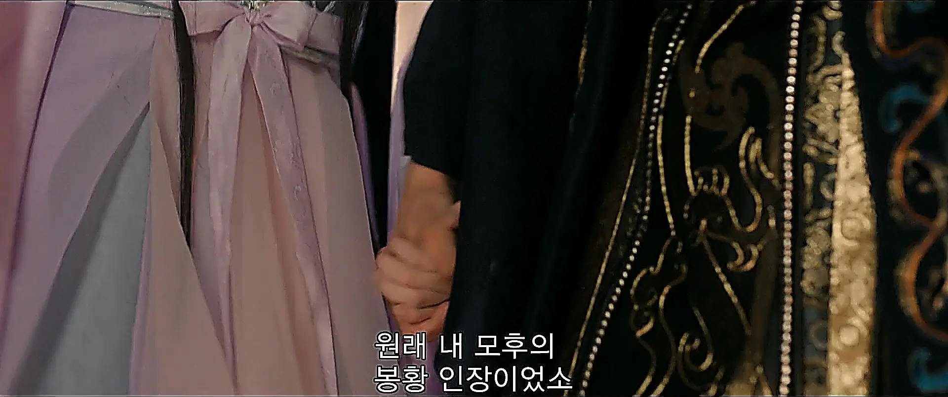 Two people holding hands, one wearing a lavender dress and the other in a dark embroidered sleeve