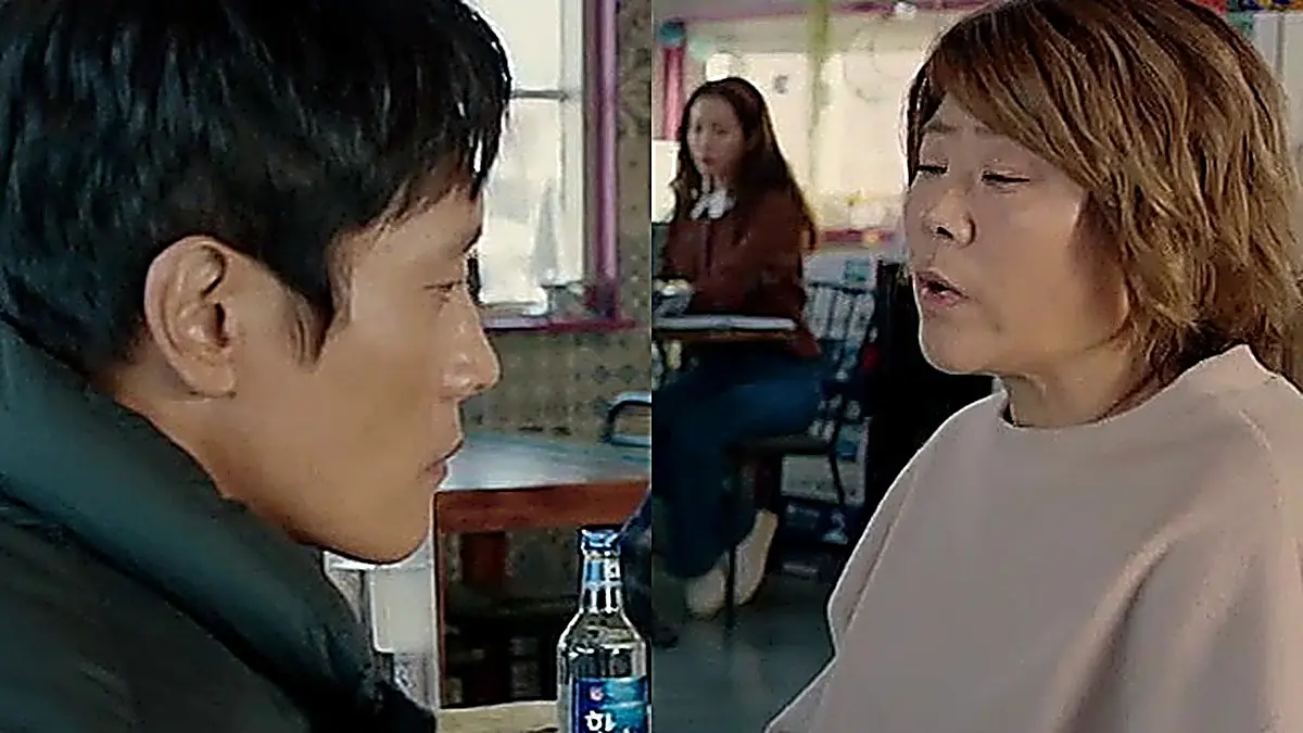 A man seated at a table across from a speaking woman in a pink sweatshirt