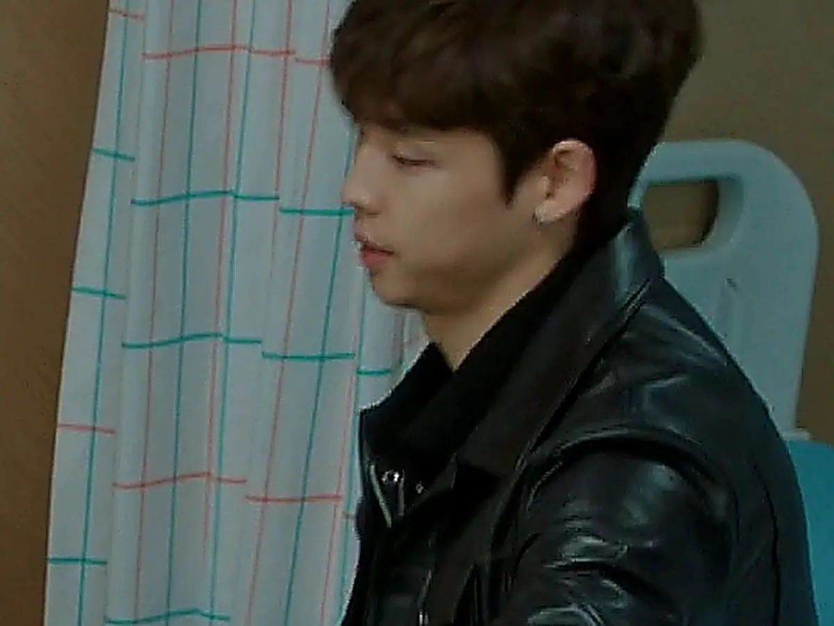 A young man wearing a black leather jacket seated beside a patterned curtain