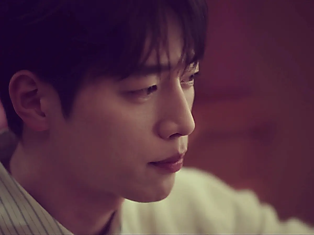 Namgung Ho in profile wearing a fine striped collared shirt under a light knit sweater