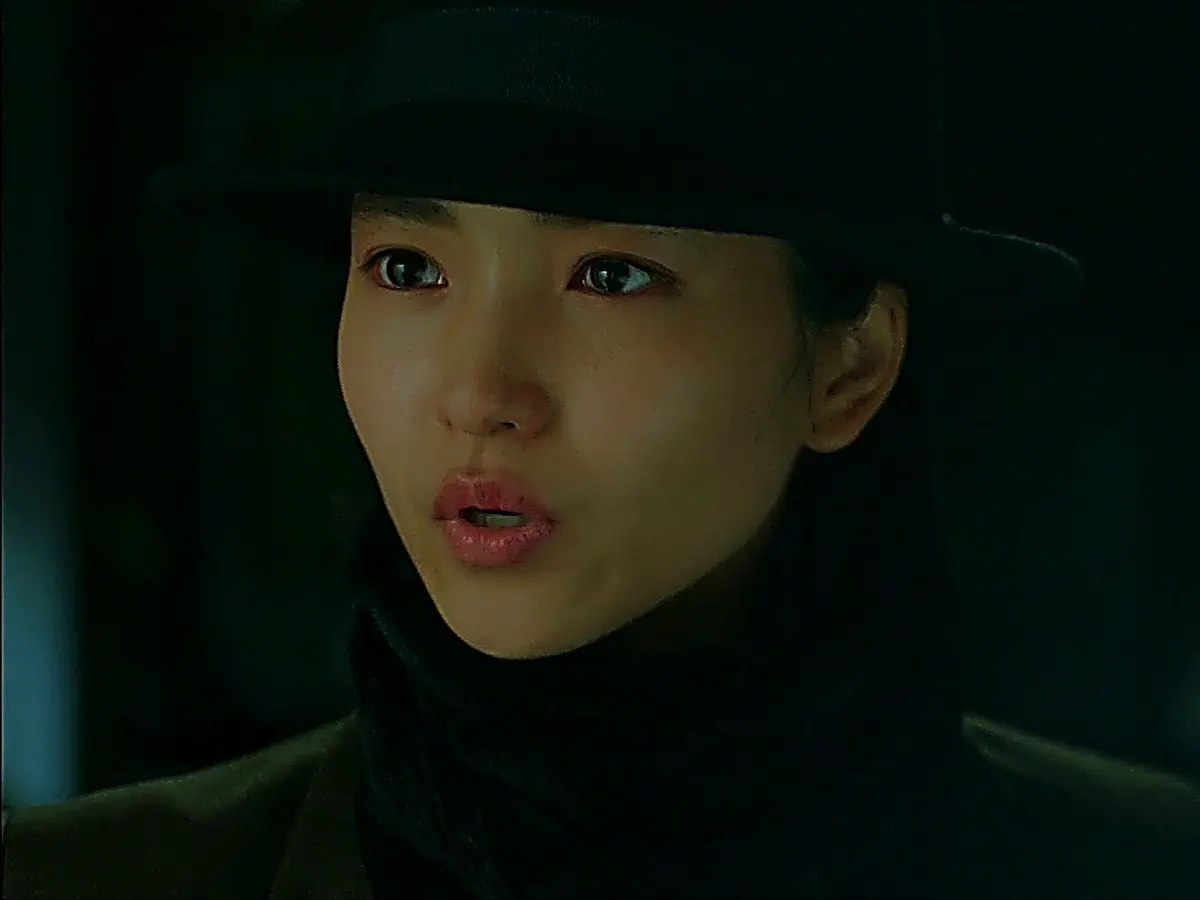 A woman in a dark brimmed hat and black scarf looking forward with a steady gaze