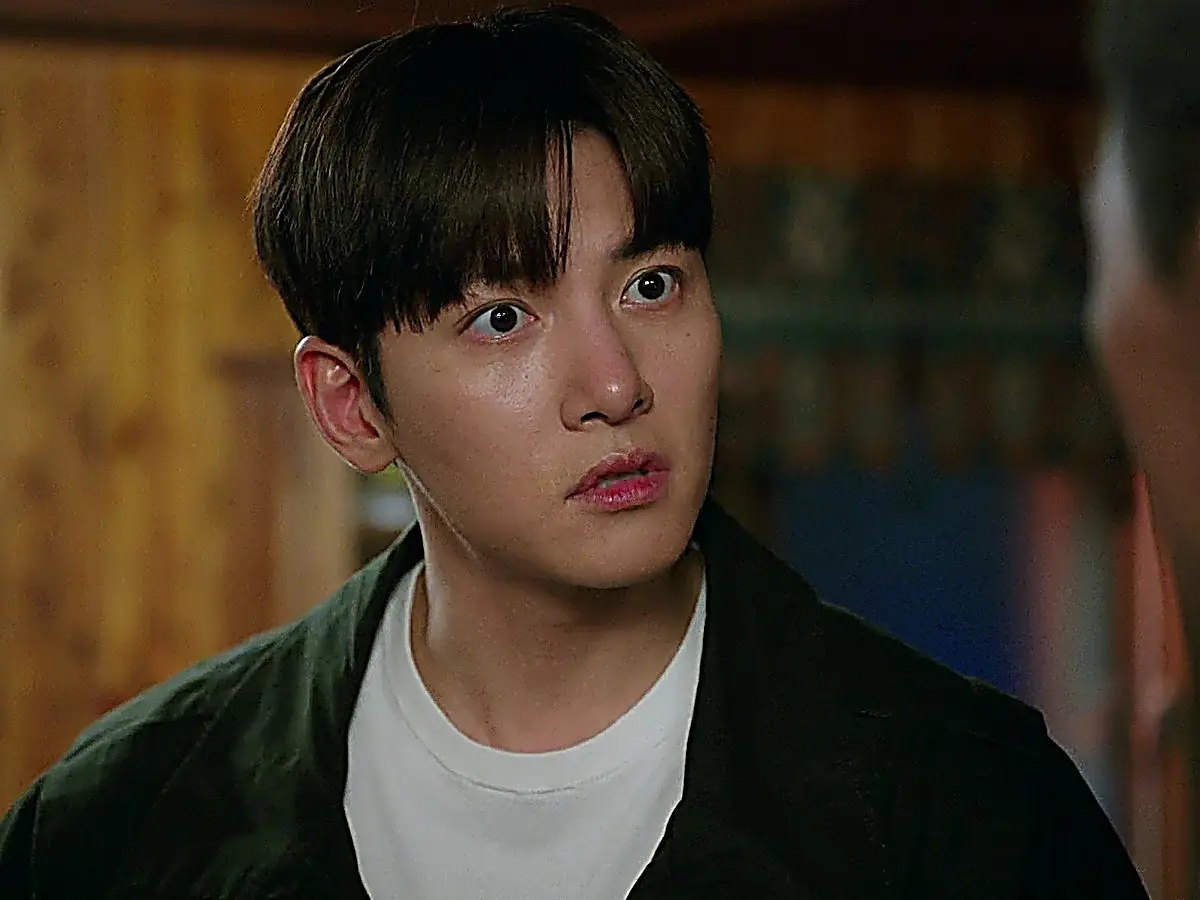 A close-up of a young man with dark hair in a white shirt and dark jacket looking surprised and hurt