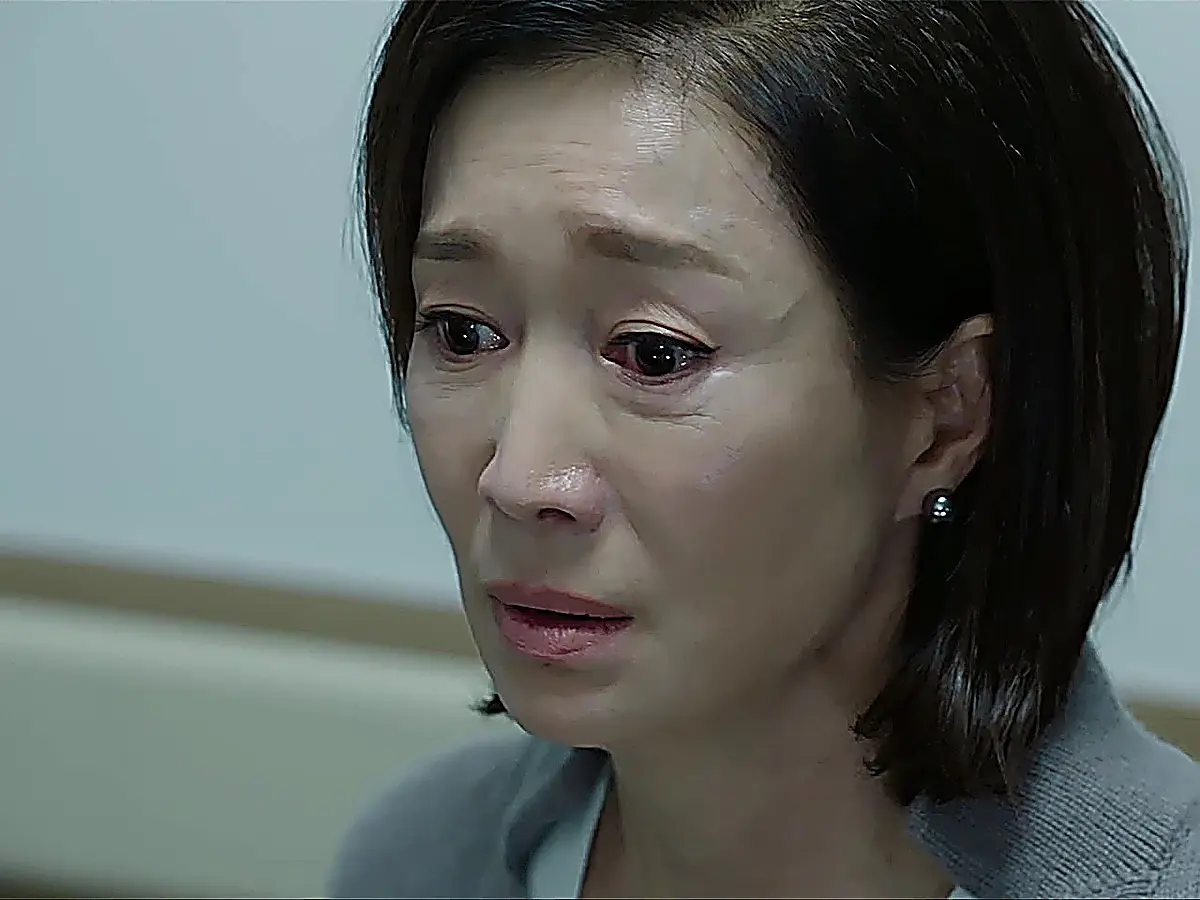 Close-up portrait of a woman with short dark hair and tear-filled eyes wearing a grey sweater