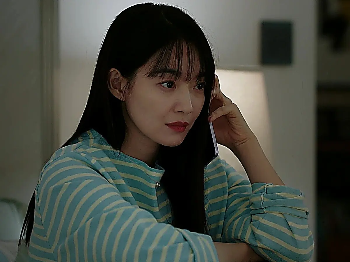 A woman with straight dark hair holding a smartphone to her ear in a striped long-sleeved shirt