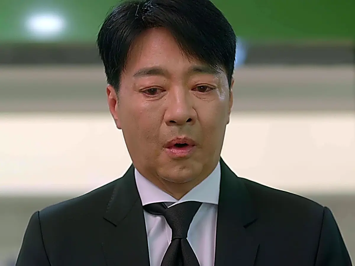Go Dae-chi in a black suit jacket, white dress shirt, and black necktie