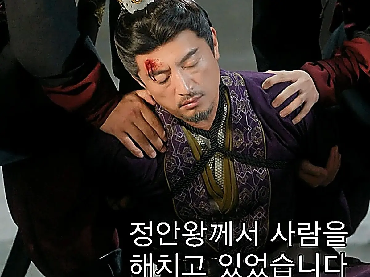 A man with blood on his forehead kneeling while restrained by figures in dark robes