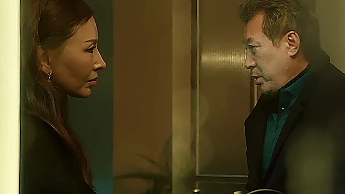 Older woman in profile facing an older man in a dark collared jacket indoors