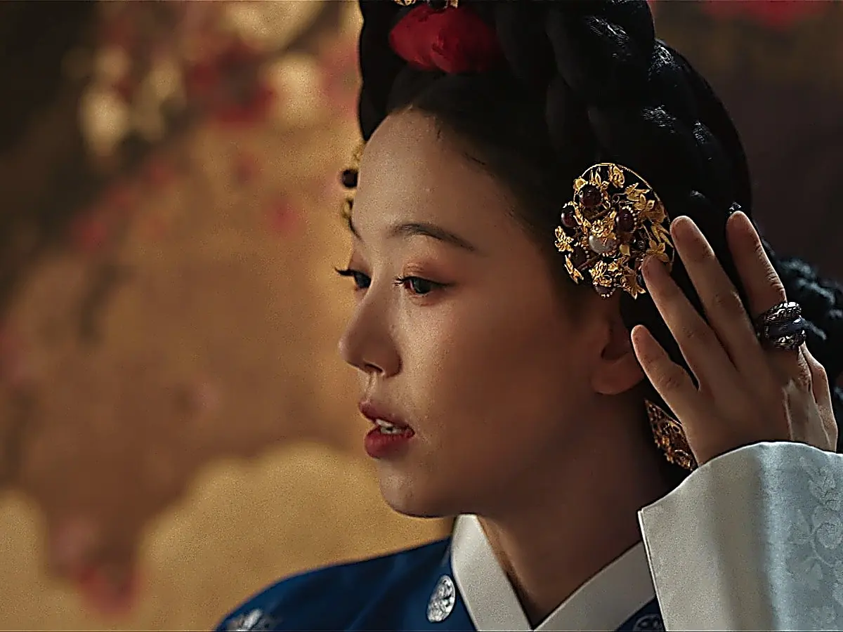 Lady Kang Mok-ju adjusting a gold floral hairpin against her dark braided wig