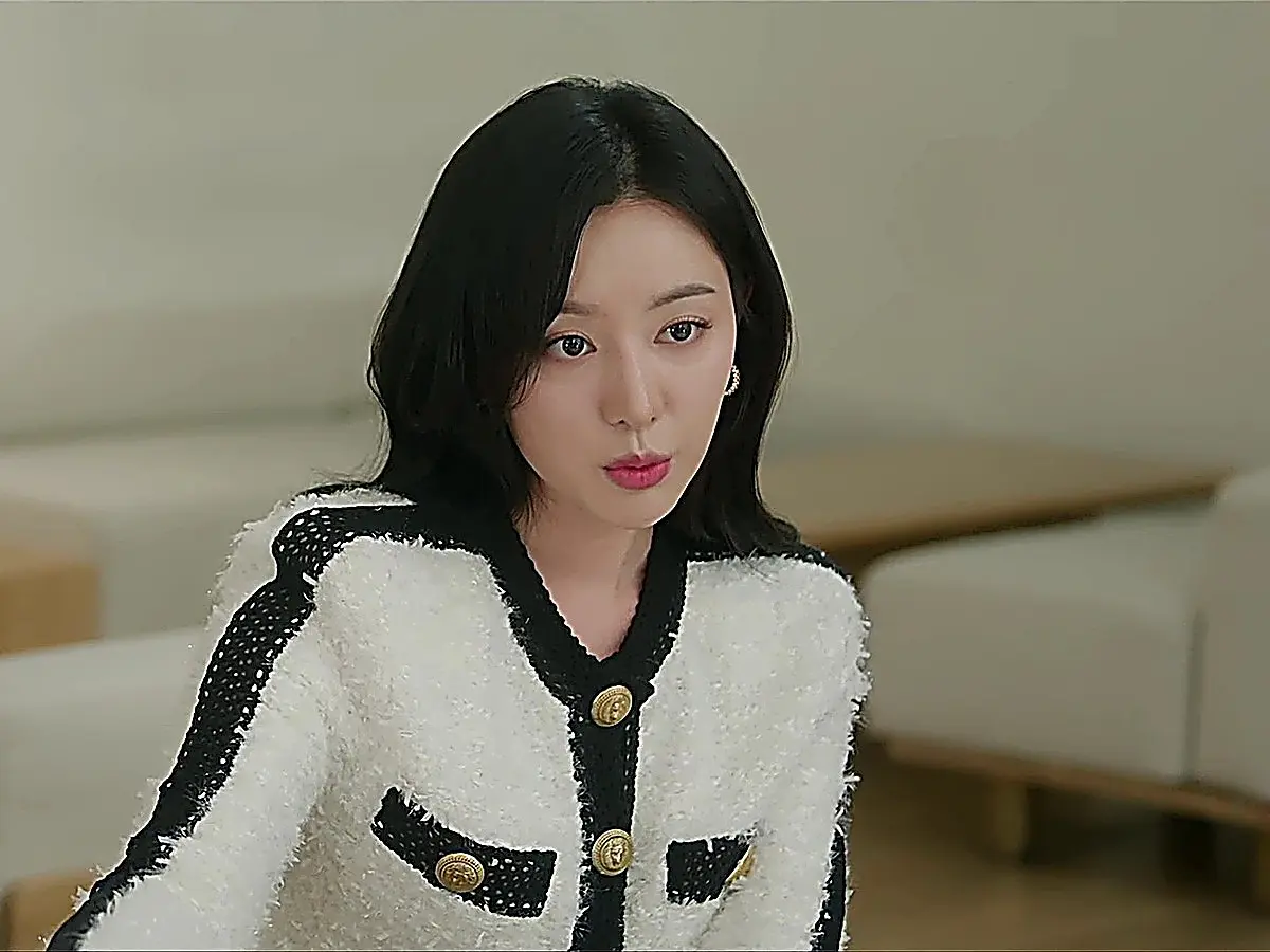 Hong Hae-in wearing a textured white jacket with black trim and gold buttons at her office desk