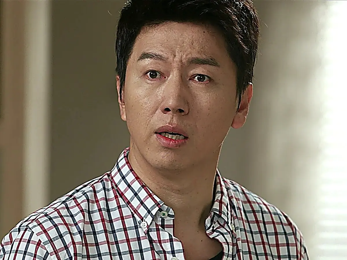 Close-up of a man wearing a plaid short-sleeve collared shirt looking forward with a wide-eyed expression