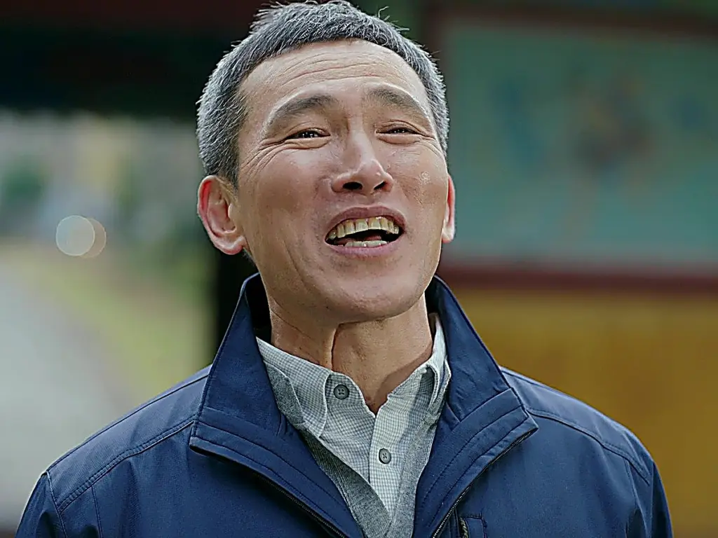 An older man with grey hair smiling warmly with tears in his eyes in a navy zip-up jacket