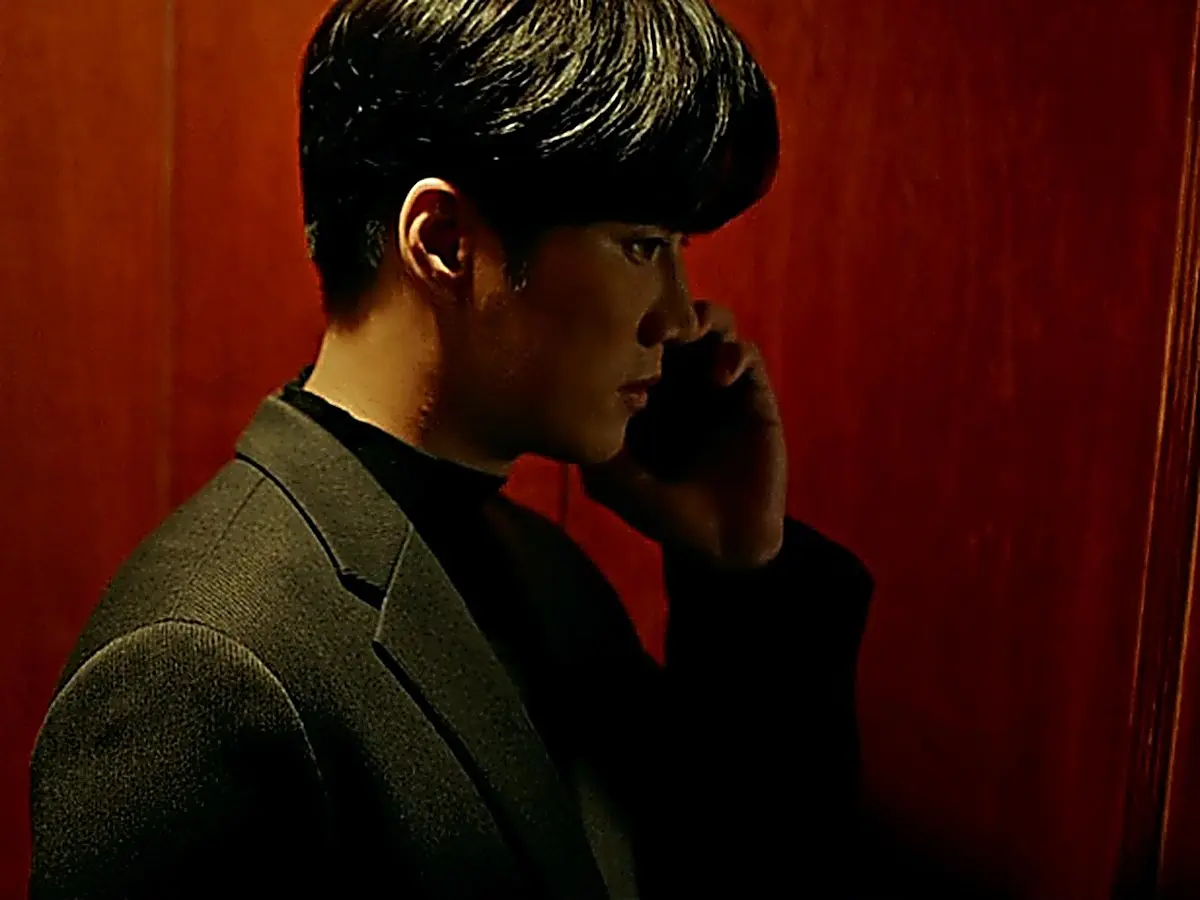 Man in profile on a phone call wearing a dark structured blazer over a black knit top