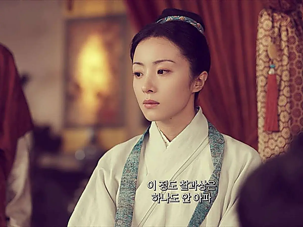 Luo Su in a pale robe accented with a patterned teal neckband