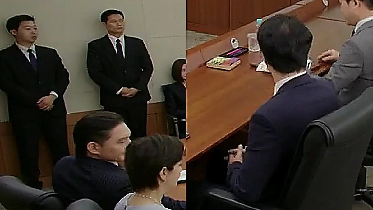 Corporate conference room with attendees in dark suits seated along a wooden boardroom table.