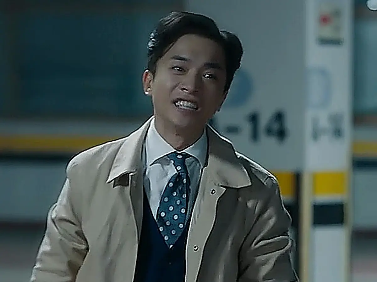 Do Jun-young wearing a beige trench coat over a collared shirt, navy knit vest, and polka-dot tie