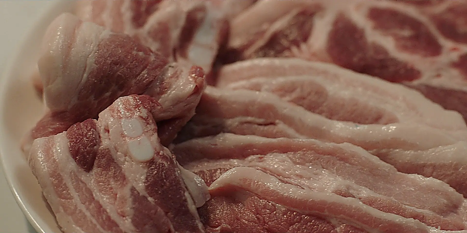 A close-up view of raw pork belly slices layered on a white plate.
